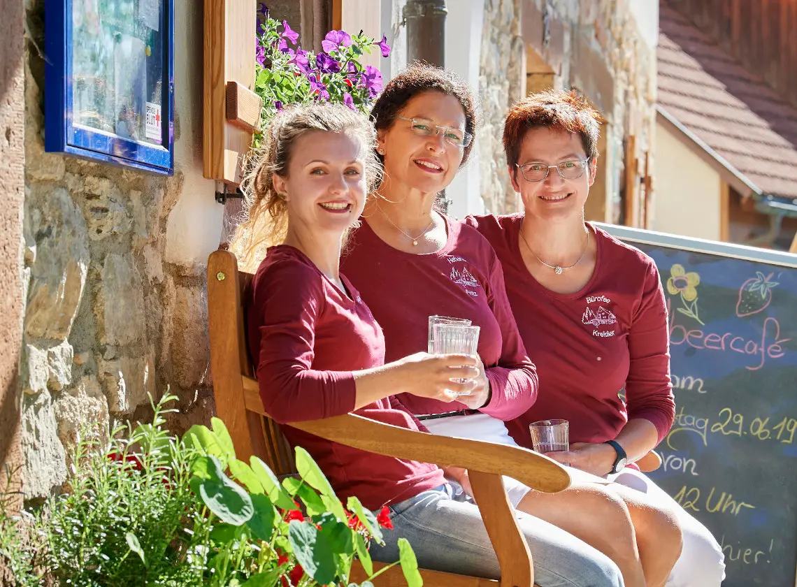 Drei Hebammen des Geburtshauses sitzen lachend auf einer Bank vor dem Haus